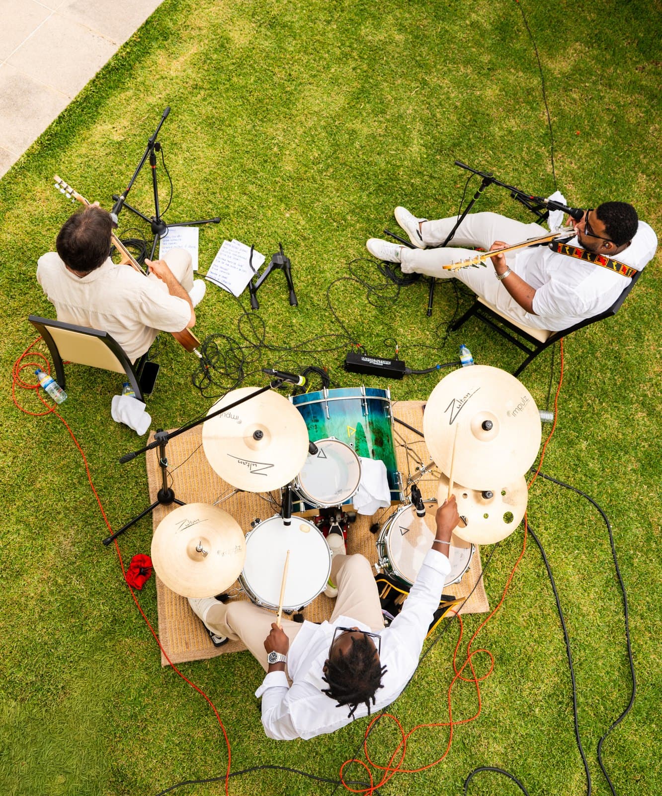 O trio visto de cima sobre a relva: a bateria ao centro, o baixo de um lado e a guitarra do outro