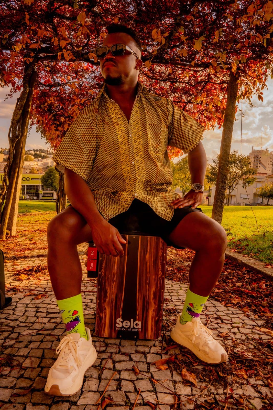 Ivirson sentado no cajón Sela num parque, debaixo de uma árvore de folhas vermelhas ao fim da tarde